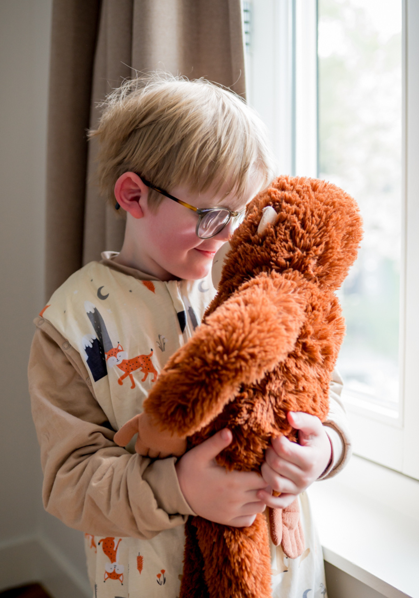 jongetje met bril in slaapzak, geeft zijn apen knuffel een knuffel.